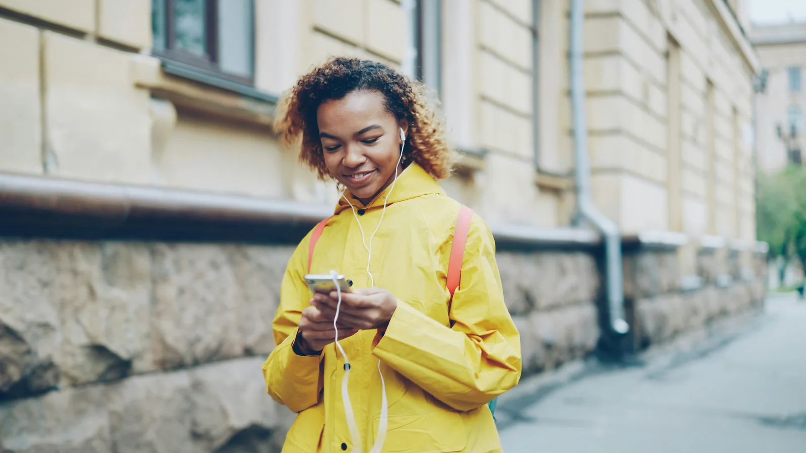 Mulher sorridente de jaqueta amarela usando um smartphone ao ar livre antes de atualizar seu perfil Instagram